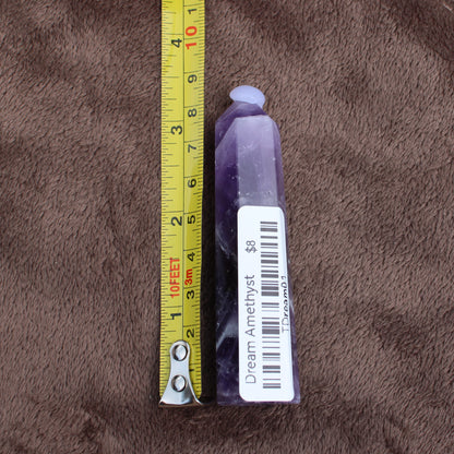 Dream Amethyst Tower crystal standing next to a measuring tape showing size on brown fabric 