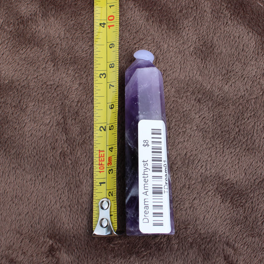 Dream Amethyst Tower crystal standing next to a measuring tape showing size on brown fabric 