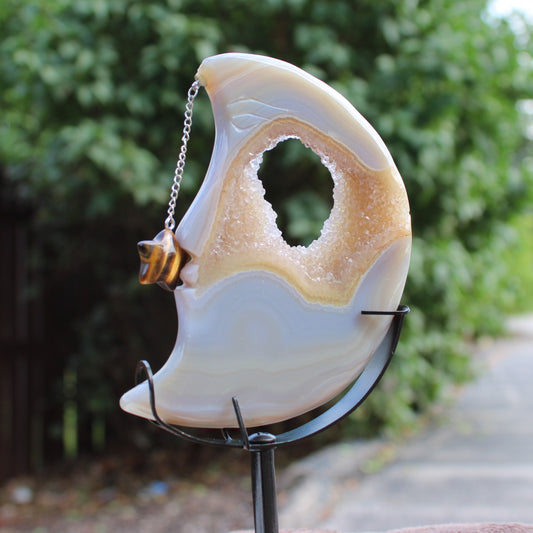 Druzy Agate Moon crystal ornament with star charm on a chain displayed on a black metal stand