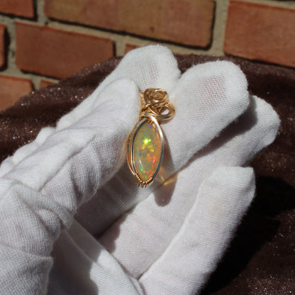 Ethiopian Opal 14k gold-filled pendant displayed on a gloved hand, featuring vibrant colors and intricate design