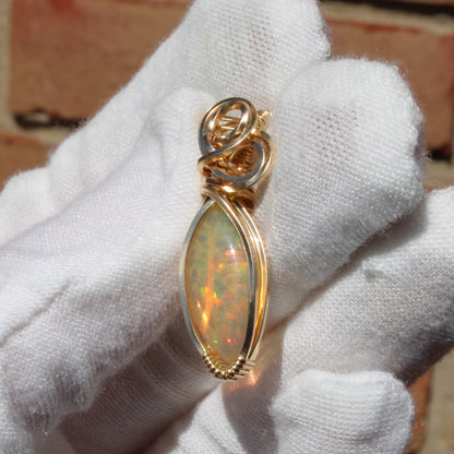Ethiopian Opal 14k gold-filled pendant elegantly displayed by a jeweler wearing white gloves