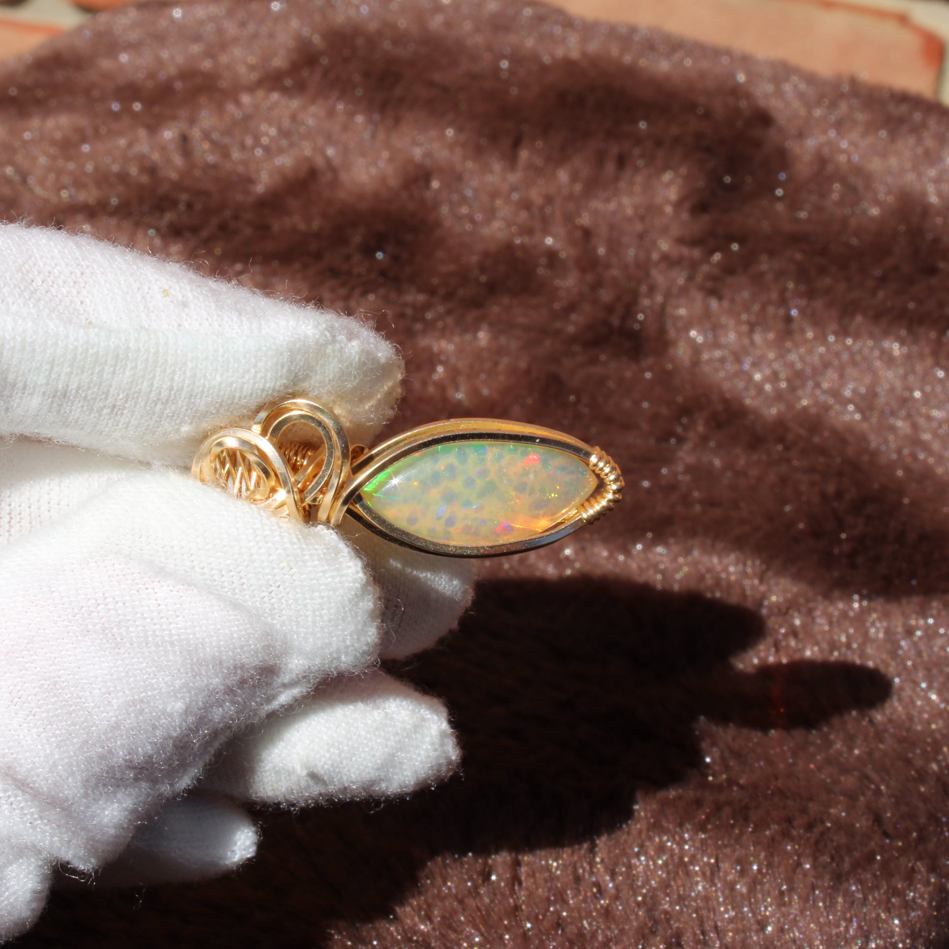 Ethiopian Opal 14k gold-filled pendant held in gloved hands for a close-up view of its unique beauty