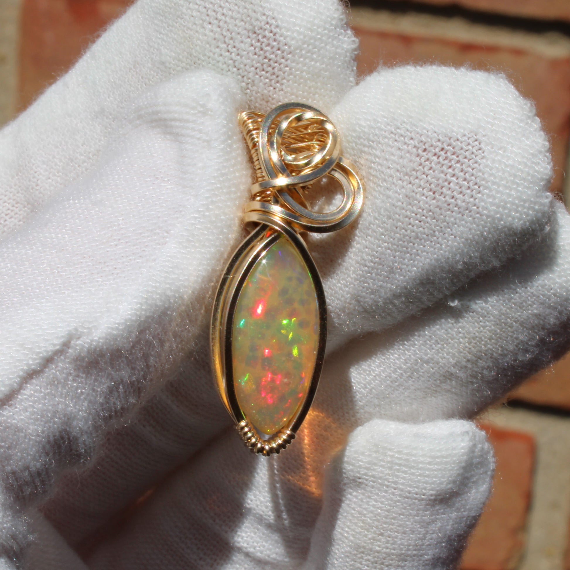 Ethiopian Opal 14k gold-filled pendant with unique color patterns held in a gloved hand