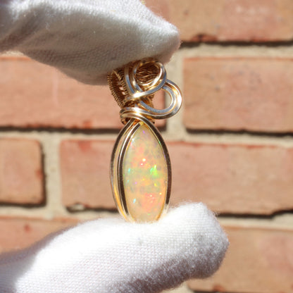 Ethiopian Opal 14k gold-filled pendant held by a gloved hand against a brick background