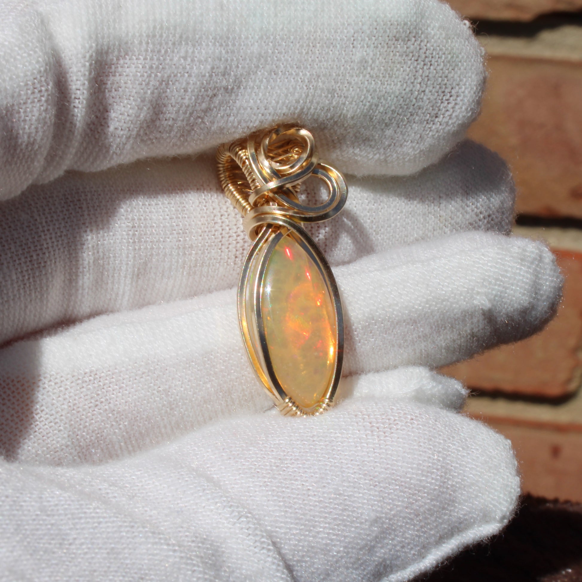 Ethiopian Opal 14k gold-filled pendant held delicately in a gloved hand showcasing its vibrant colors