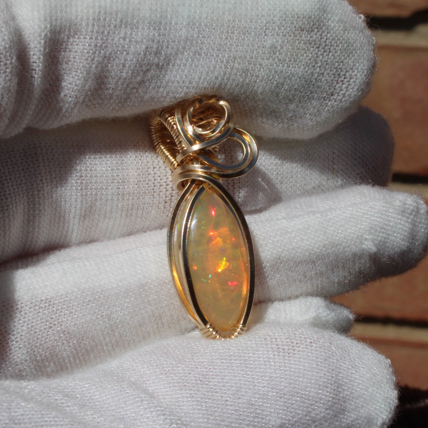 Ethiopian Opal 14k gold-filled pendant displayed on a hand with a white glove for elegant presentation