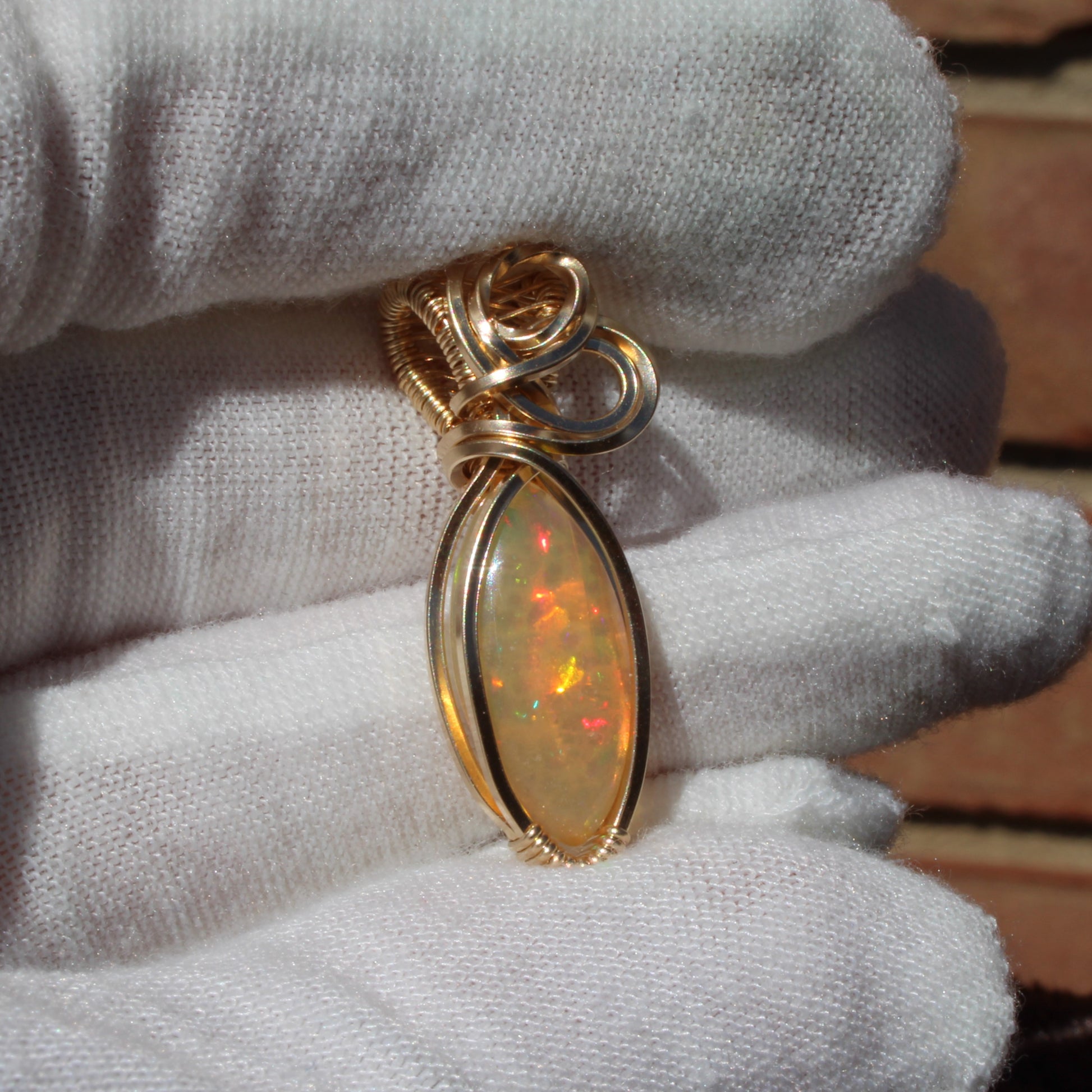 Ethiopian Opal 14k gold-filled pendant displayed on a hand with a white glove for elegant presentation