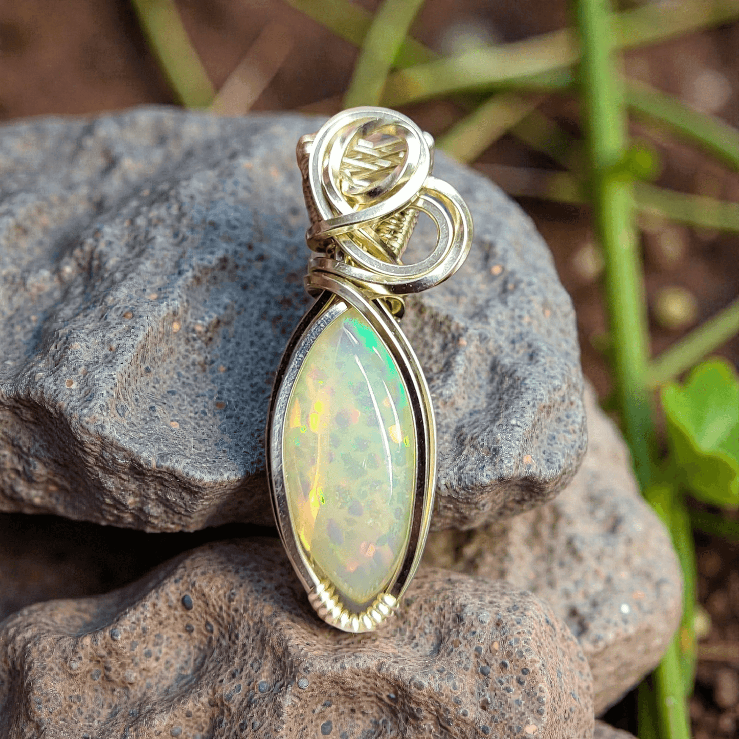 Ethiopian Opal 14k gold-filled pendant with intricate wire design resting on textured stones