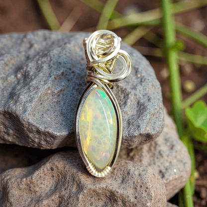 Ethiopian Opal 14k gold-filled pendant with intricate wire design resting on textured stones