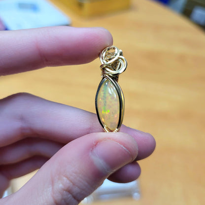 Ethiopian Opal 14k gold-filled pendant elegantly held between fingers, showcasing vibrant colors and intricate design