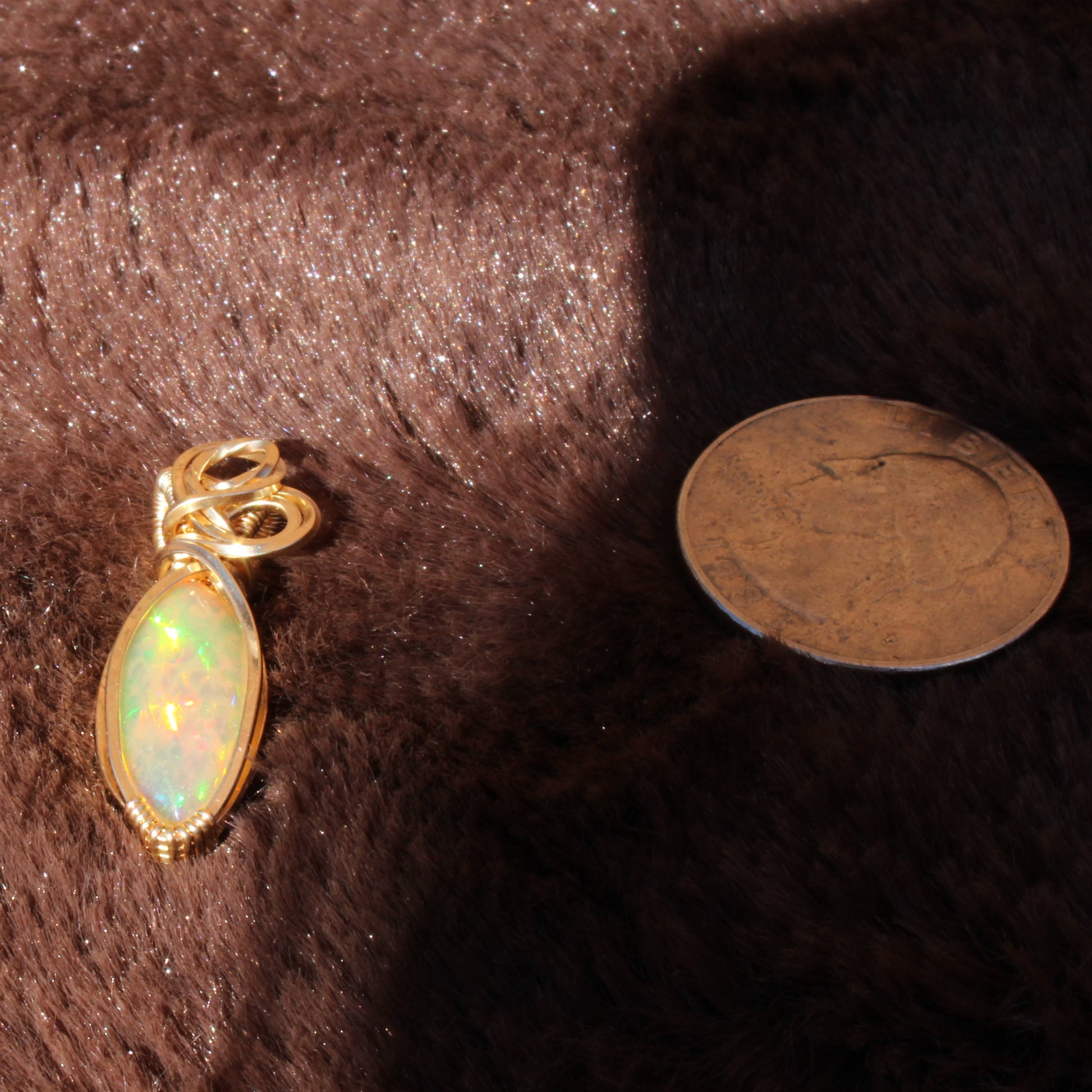 Ethiopian Opal 14k gold-filled pendant displayed on a soft surface with a coin for size reference