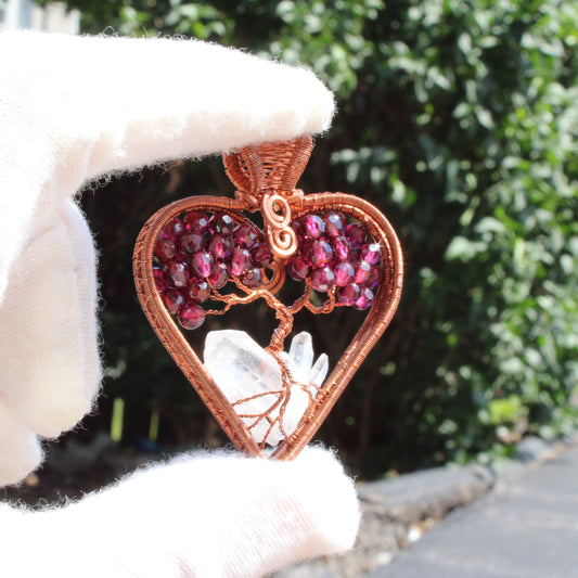 Garnet heart tree of life pendant with a crystal base, held by a gloved hand outdoors