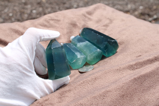 Hand holding a green fluorite tower among various other green fluorite pieces with a coin for size reference