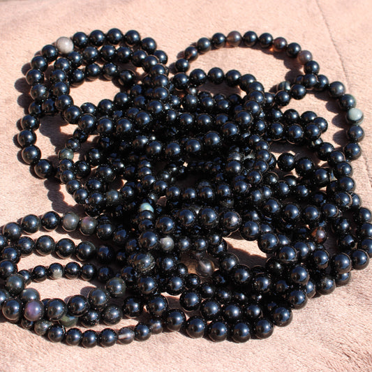 Handmade obsidian bracelet displayed in a tangled arrangement showcasing polished black beads