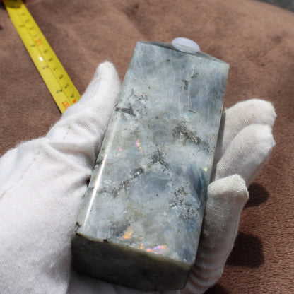 Labradorite Tower crystal held in gloved hand showing its smooth polished surface and iridescent colors