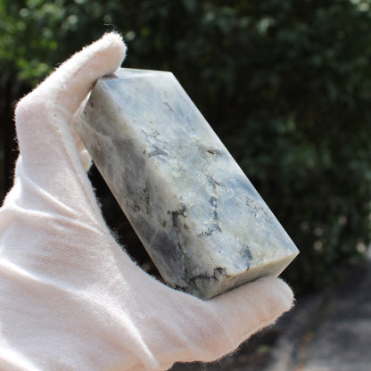 Hand holding a polished Labradorite Tower crystal with natural gray and blue hues outdoors