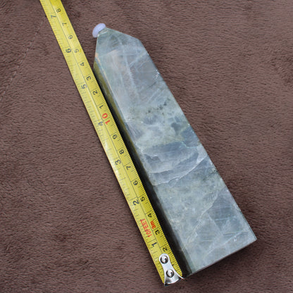 Labradorite Tower crystal standing next to a measuring tape on brown fabric background