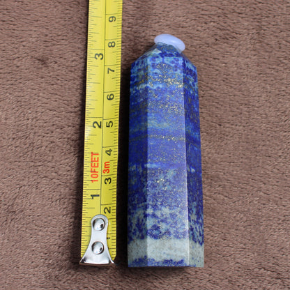 Lapiz Lazuli Tower crystal standing next to a tape measure showing its size on a brown textured surface