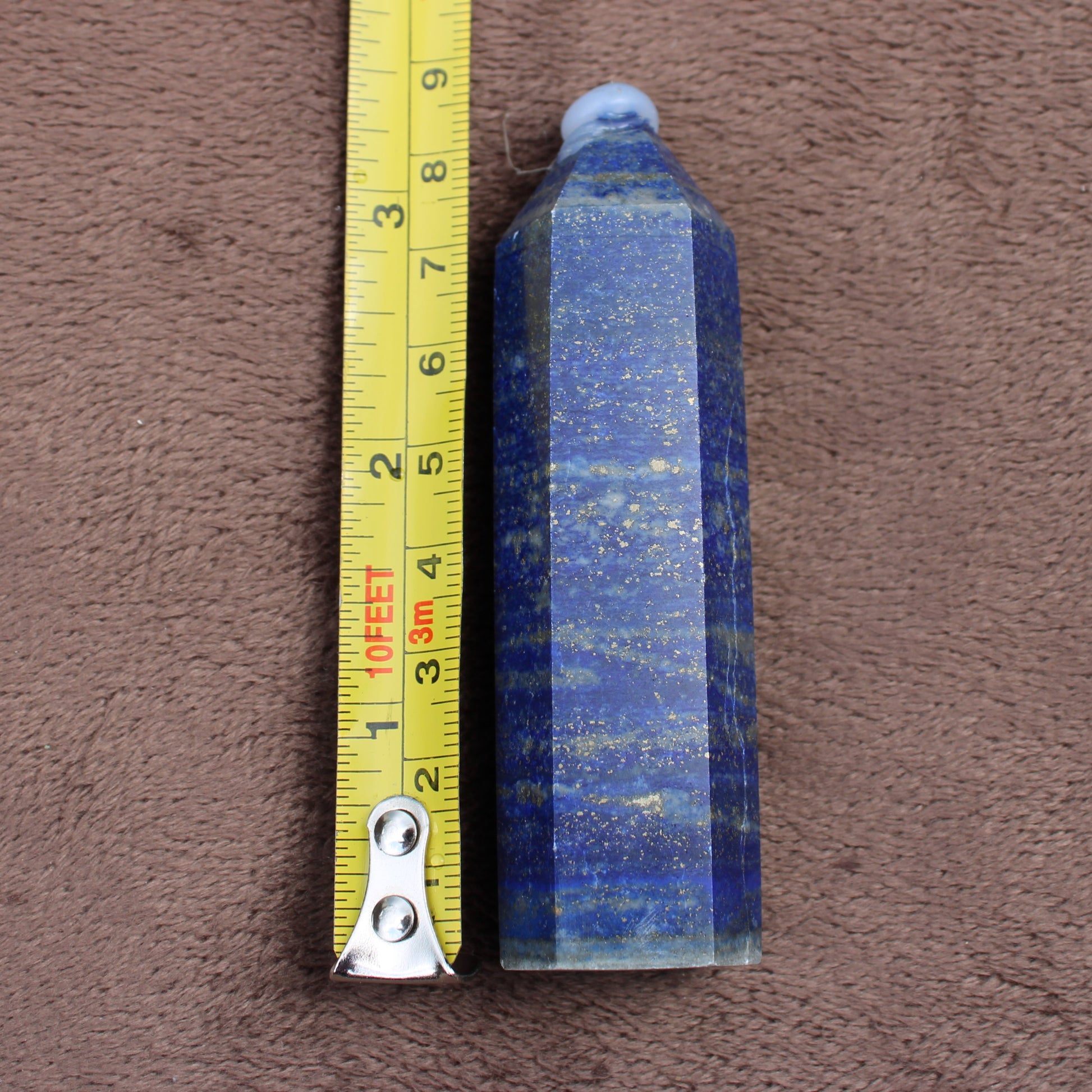 Lapiz Lazuli Tower crystal with deep blue and gold flecks beside a yellow measuring tape