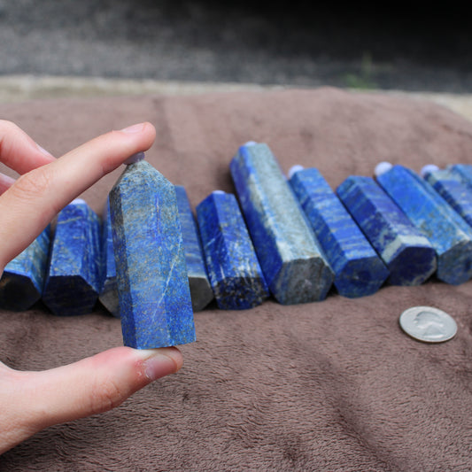 Hand holding a polished Lapiz Lazuli Tower crystal with multiple blue Lapiz Lazuli Towers displayed on a brown cloth