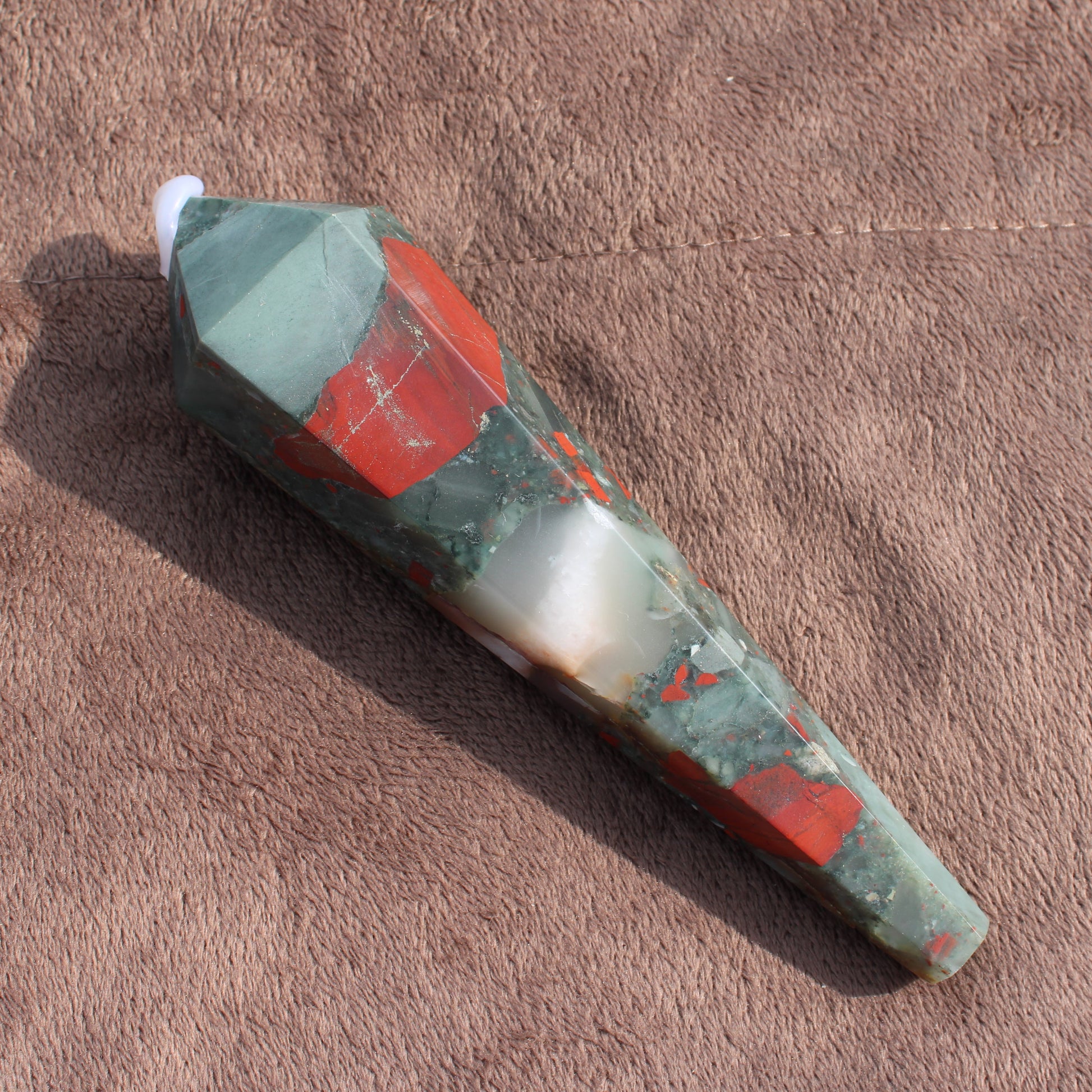 Large Bloodstone Wand crystal with green and red hues on brown fabric background