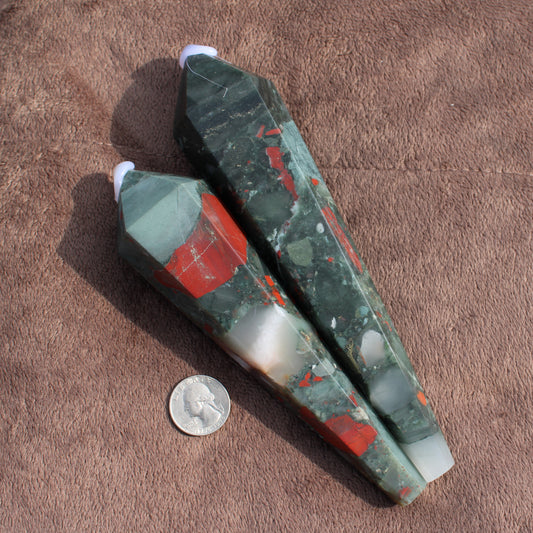 Two polished Large Bloodstone Wands with green and red patterns displayed on brown fabric next to a quarter for size comparison