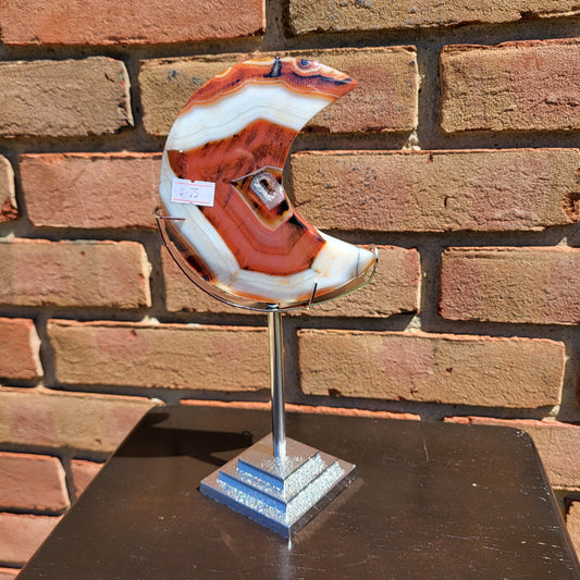 Large red agate moon sculpture displayed on a stand, showcasing vibrant patterns and colors