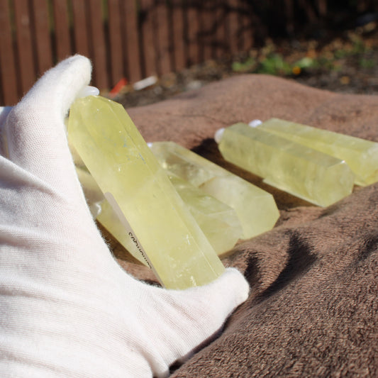 Lemon Quartz Tower held in hand with multiple towers on a brown surface for display
