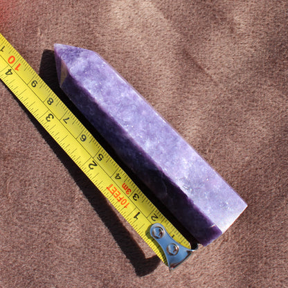 Lepidolite Tower crystal next to a yellow measuring tape on a brown surface