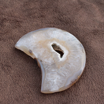 Little Agate Moon crystal with natural translucent white and beige tones on a brown textured surface