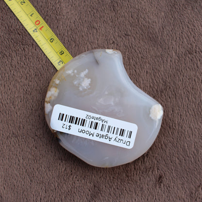 Little Agate Moon crystal from Different Branches LLC with milky white and beige patterns shown next to measuring tape