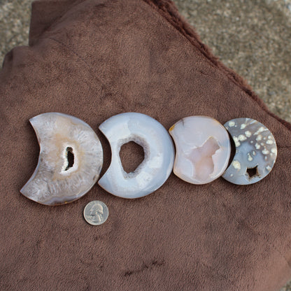 Different Branches LLC Little Agate Moon crystal slices in various colors displayed on brown fabric with quarter for size reference