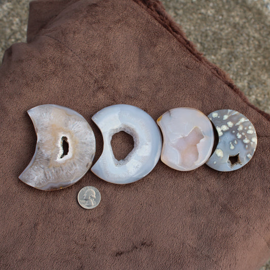 Different Branches LLC Little Agate Moon crystal slices in various colors displayed on brown fabric with quarter for size reference
