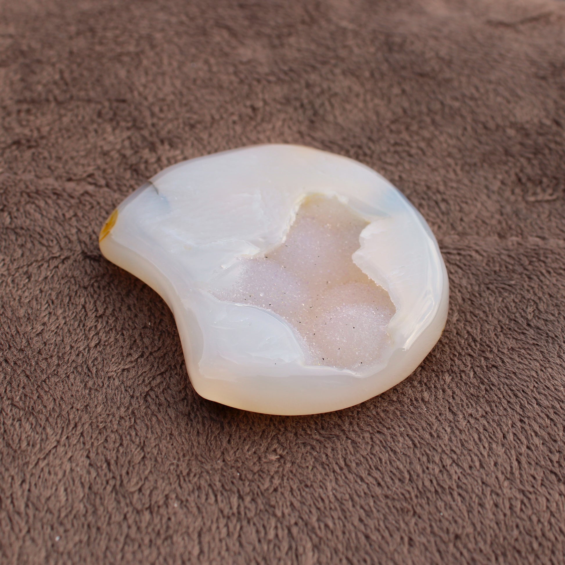 Different Branches LLC Little Agate Moon crystal with white and beige tones on brown fabric