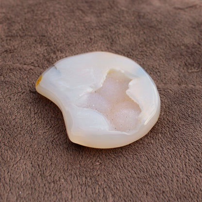 Different Branches LLC Little Agate Moon crystal with white and beige tones on brown fabric