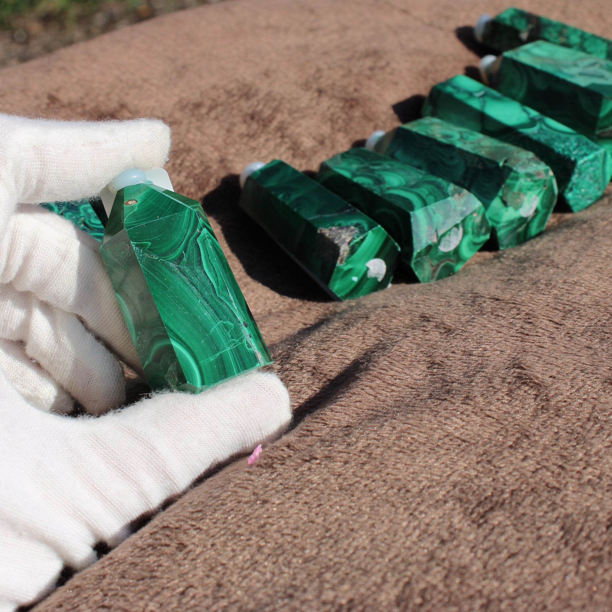 Hand holding a shimmering Malachite tower from the Malachite tower collection on a soft surface