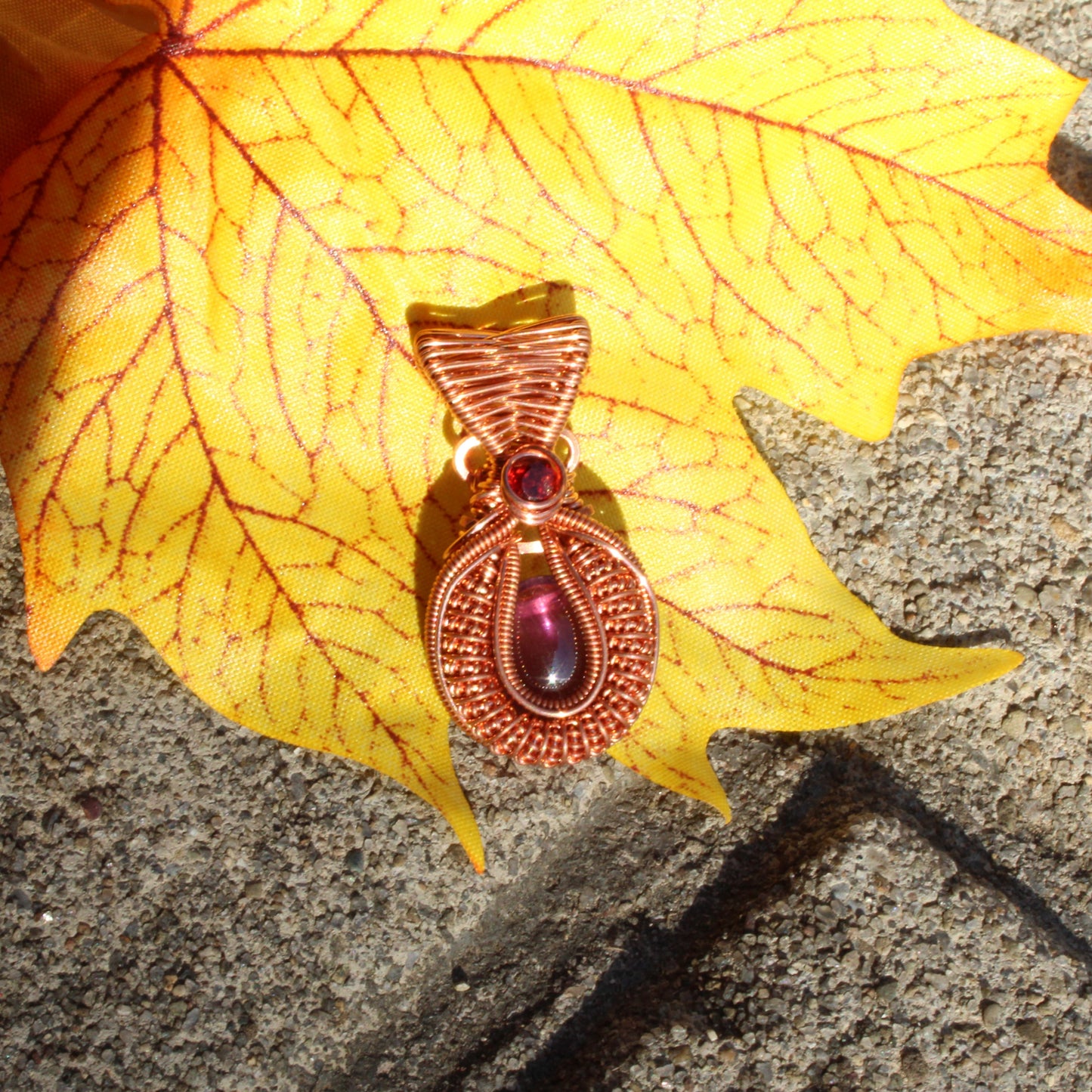Mini amethyst copper pendant featuring intricate design and vibrant purple stone on a decorative leaf background