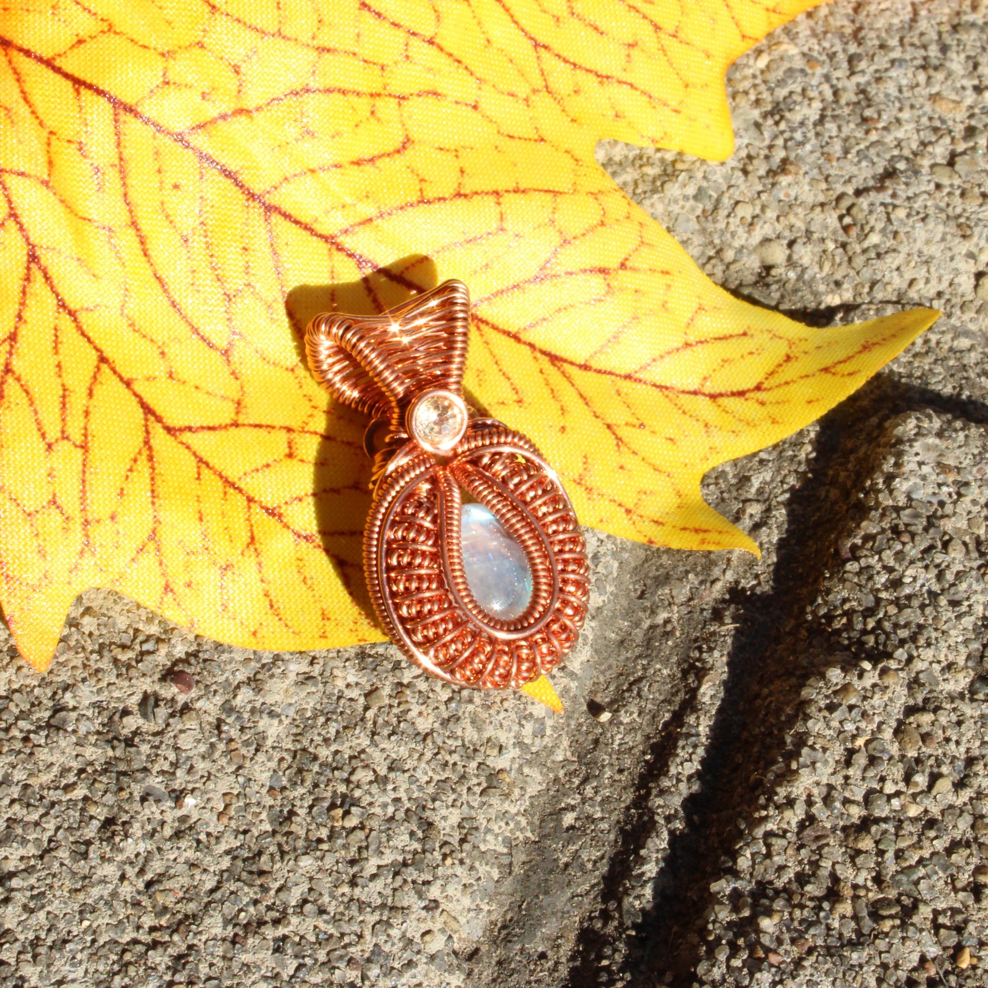 Mini rainbow moonstone copper pendant with intricate design on a vibrant leaf background