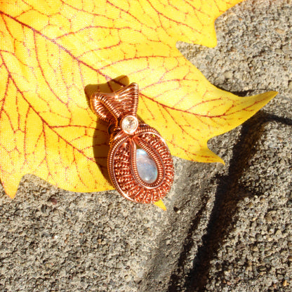 Mini rainbow moonstone copper pendant with intricate design on a vibrant leaf background