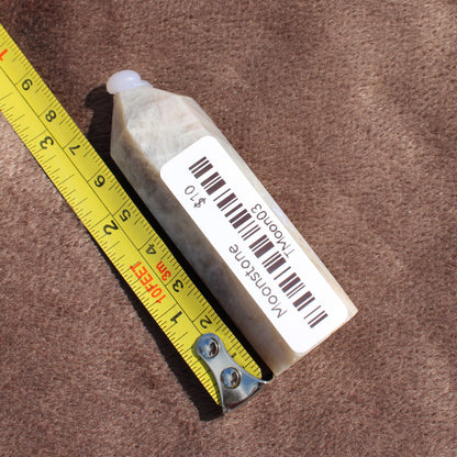 Moonstone Tower crystal from Different Branches LLC placed next to a yellow measuring tape on brown fabric