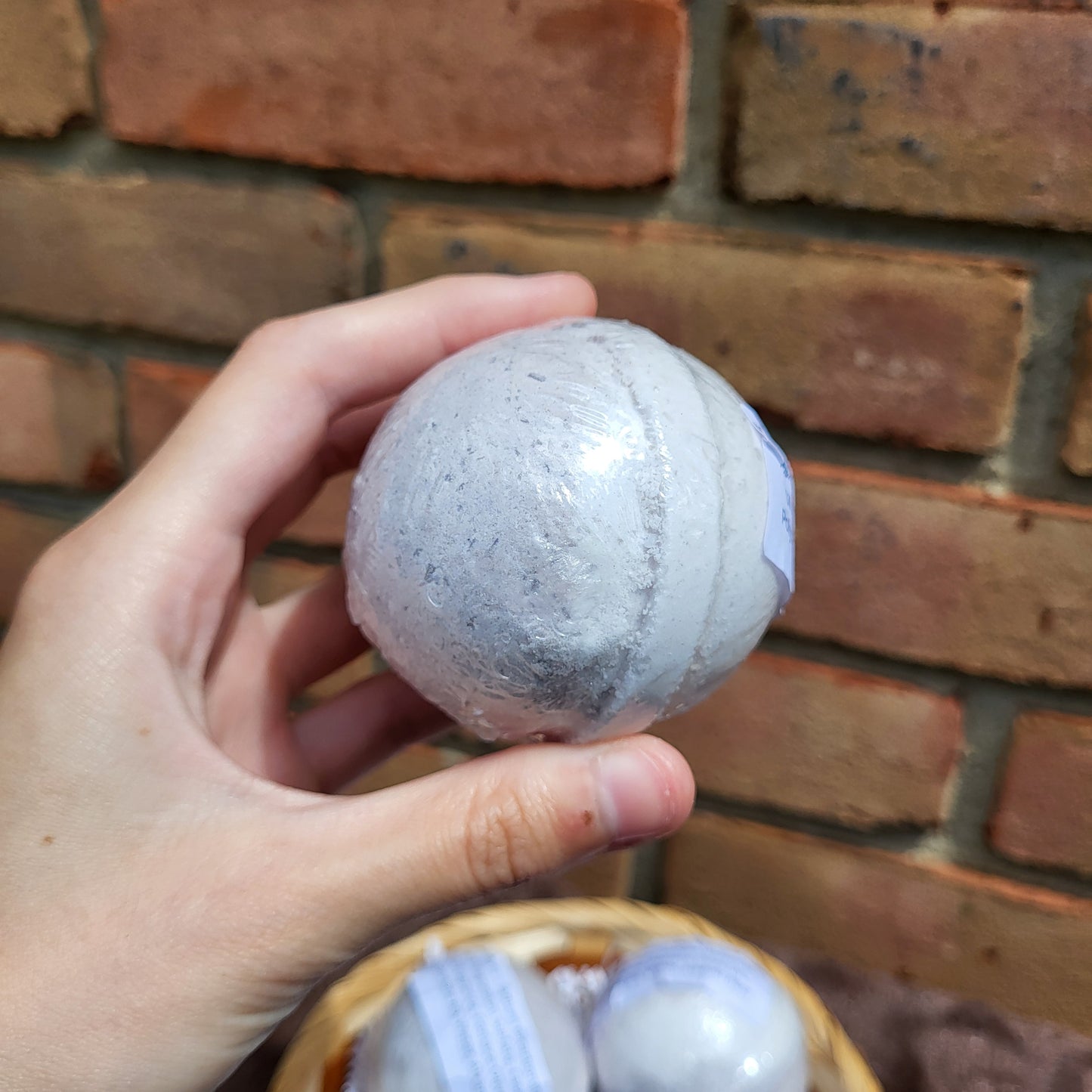 Hand holding a Made Natural bath bomb in lavender, frankincense & clary sage with natural color