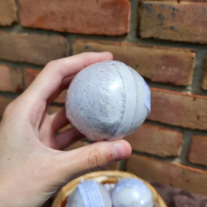 Hand holding a Made Natural bath bomb in lavender, frankincense & clary sage with natural color