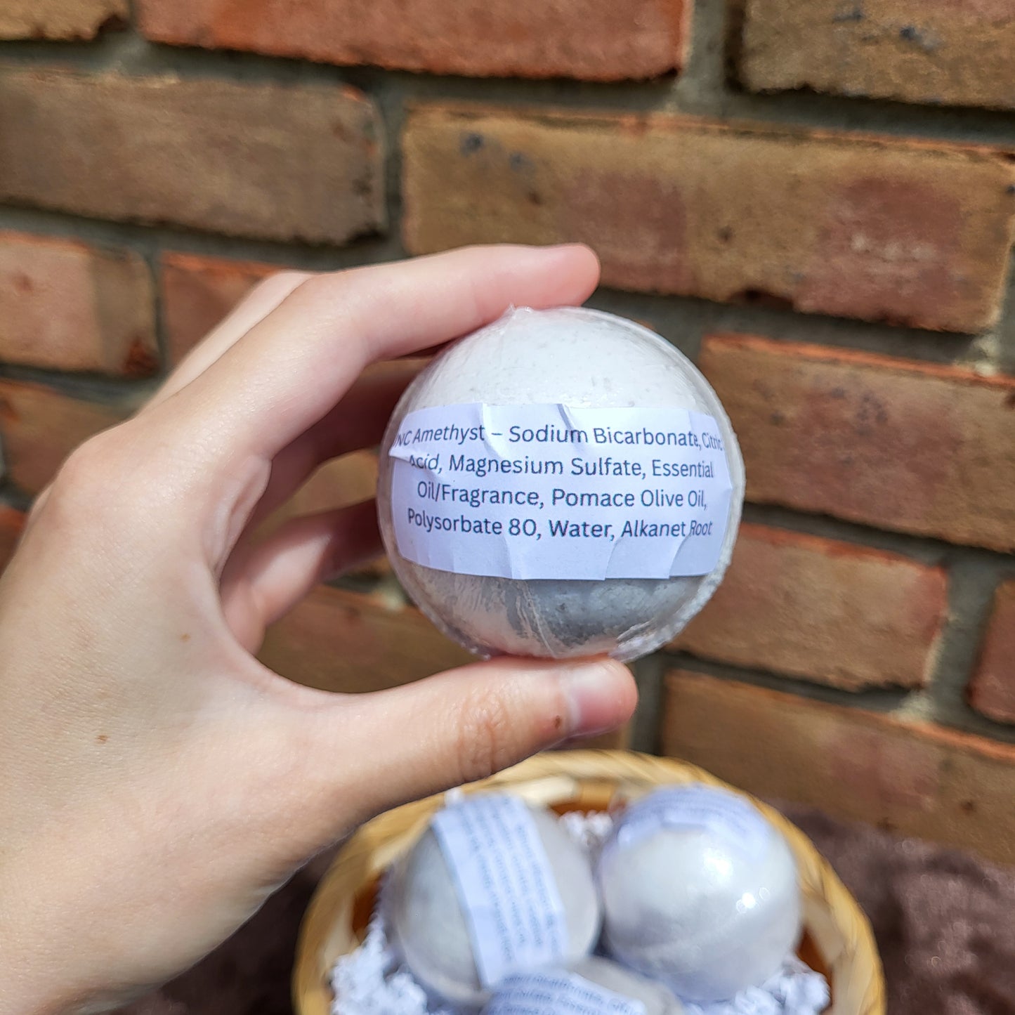 Hand holding a Made Natural bath bomb labeled with Natural Color Lavender, Frankincense & Clary Sage ingredients