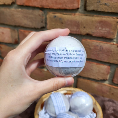 Hand holding a Made Natural bath bomb labeled with Natural Color Lavender, Frankincense & Clary Sage ingredients