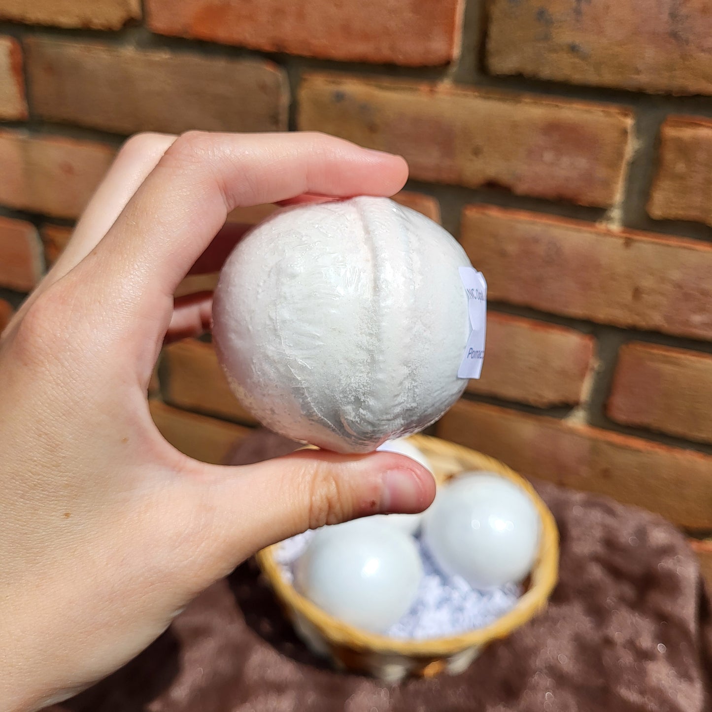 Hand holding a Made Natural bath bomb in white, featuring Natural Color Lavender, Sweet Orange & Clary Sage scent