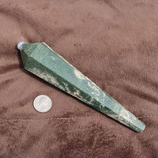 Green and white polished Moss Agate Wand crystal next to a quarter for size comparison