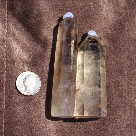 Two polished Smokey Quartz Tower crystals next to a quarter for size reference on a brown fabric background