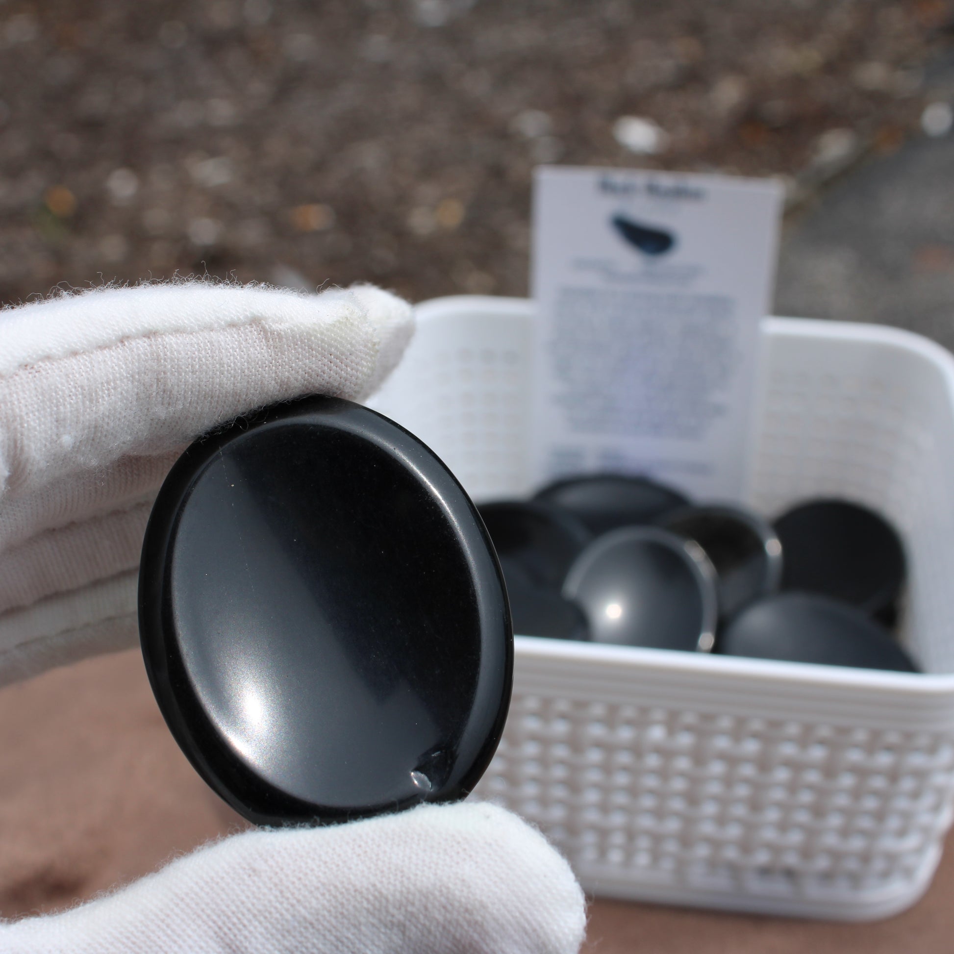 Obsidian Worry Stone held by gloved hand with more stones in white basket by Different Branches LLC