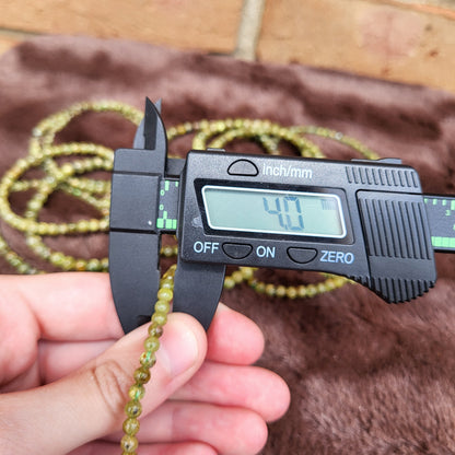 Measuring Peridot bracelet beads with calipers for precise sizing and quality assurance