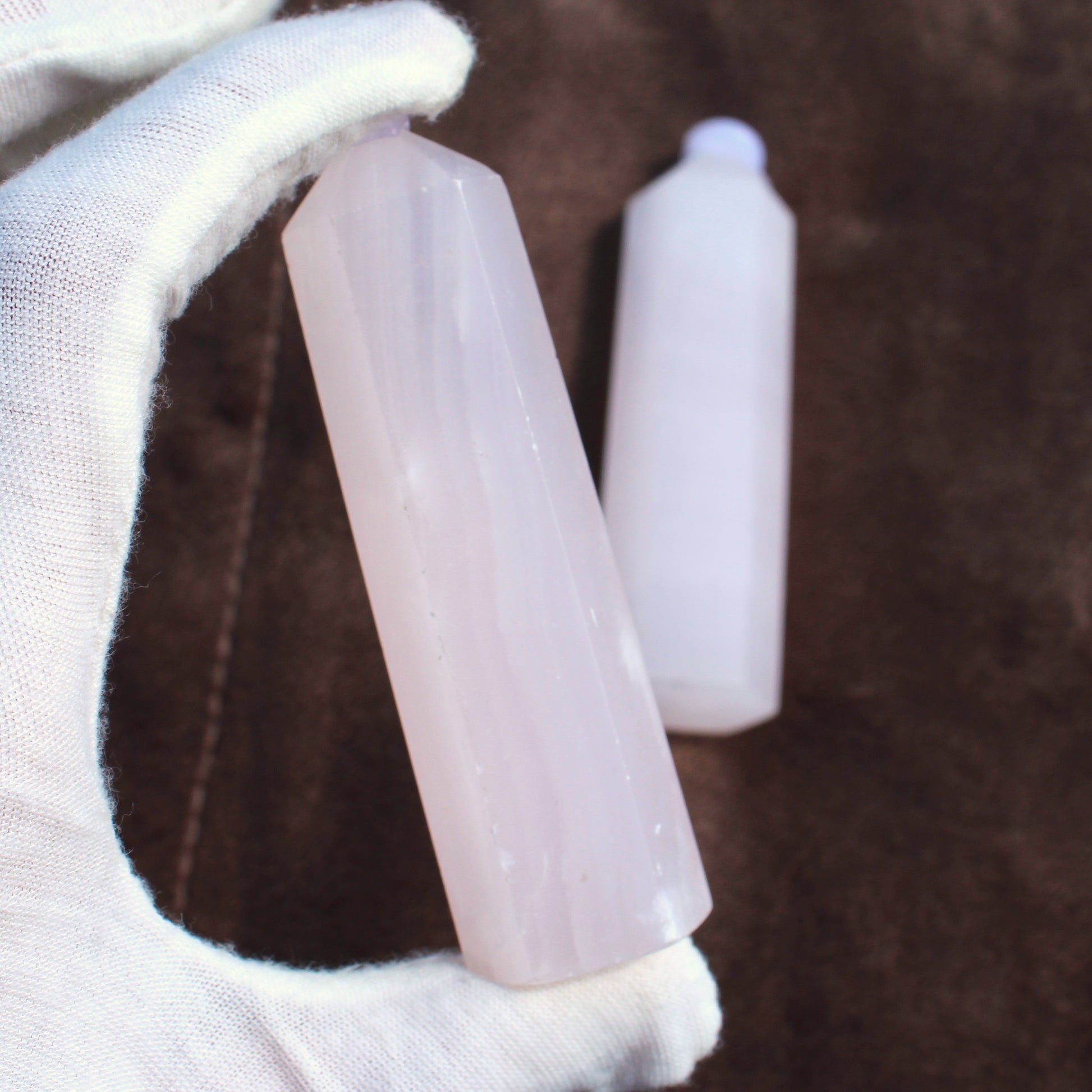 Hand holding a polished Pink Calcite Tower crystal with a brown background